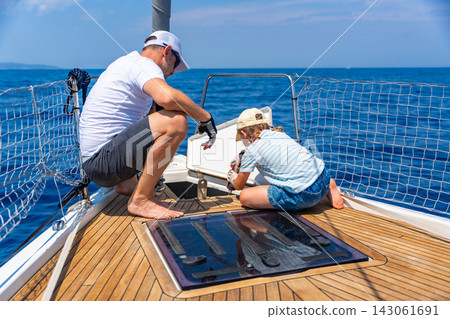 Father teaching his daughter basic yacht maintenance during a family sailing trip. Learning practical sailing skills, teamwork and confidence through shared outdoor experience. Father teaching his daughter basic yacht maintenance during a family sailing trip. Learning practical sailing skills, teamwork and confidence through shared outdoor experience. 143061691