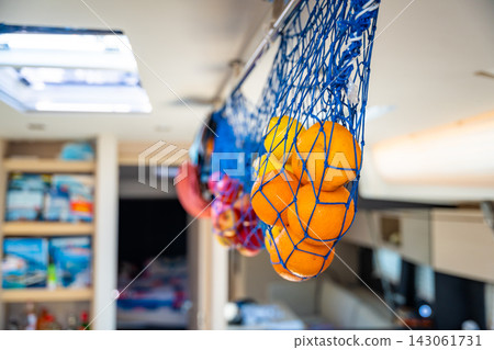 Fresh oranges and other citrus fruits stored in a hanging net inside a yacht galley during a sailing trip. Concept of healthy nutrition, vitamin supply, food storage, self-sufficient cruising Fresh oranges and other citrus fruits stored in a hanging net inside a yacht galley during a sailing trip. Concept of healthy nutrition, vitamin supply, food storage, self-sufficient cruising 143061731