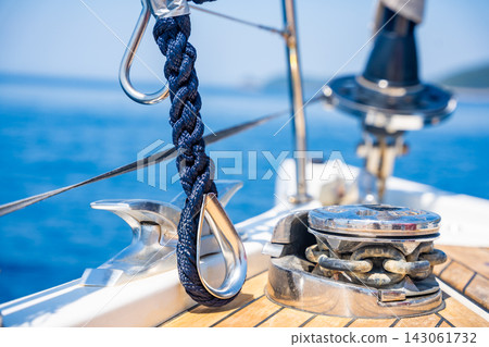 Mooring rope secured to a stainless steel cleat on the deck of a modern sailing yacht. Safe docking equipment and seamanship concept. Mooring rope secured to a stainless steel cleat on the deck of a modern sailing yacht. Safe docking equipment and seamanship concept. 143061732