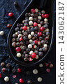 Variety of colorful peppercorns in a black spoon on dark textured surface. 143062187