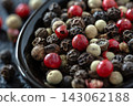 Close-up of mixed peppercorns in a black bowl on a textured surface. 143062188