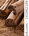 Close-up of cinnamon sticks on ground cinnamon powder in warm lighting. 143062189