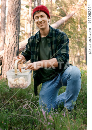 Man foraging wild mushrooms in the forest, holding a knife and basket full of bolete mushrooms, gathering seasonal harvest during an autumn outdoor activity. Man foraging wild mushrooms in the forest, holding a knife and basket full of bolete mushrooms, gathering seasonal harvest during an autumn outdoor activity. 143062964
