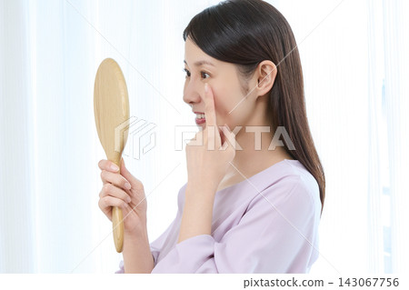 一位女士對著鏡子檢查自己的臉部狀況。 一位女士對著鏡子檢查自己的臉部狀況。 143067756
