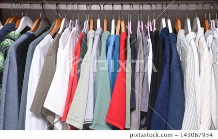 view of a organized wardrobe featuring a varied selection of men casual garments suspended on a metal handing rod. 143067934