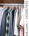 view of a organized wardrobe featuring a varied selection of men casual garments suspended on a metal handing rod. 143067935