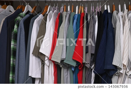 view of a organized wardrobe featuring a varied selection of men casual garments suspended on a metal handing rod. view of a organized wardrobe featuring a varied selection of men casual garments suspended on a metal handing rod. 143067936