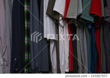 view of a organized wardrobe featuring a varied selection of men casual garments suspended on a metal handing rod. 143067937