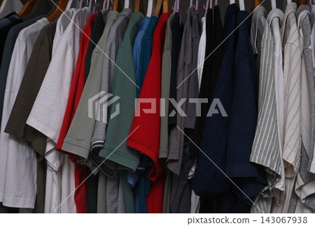 view of a organized wardrobe featuring a varied selection of men casual garments suspended on a metal handing rod. view of a organized wardrobe featuring a varied selection of men casual garments suspended on a metal handing rod. 143067938