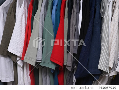 view of a organized wardrobe featuring a varied selection of men casual garments suspended on a metal handing rod. view of a organized wardrobe featuring a varied selection of men casual garments suspended on a metal handing rod. 143067939