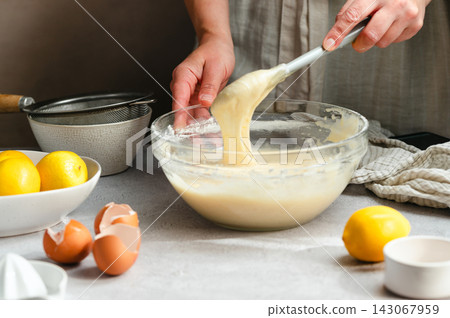 Woman whisking lemon cake batter in a glass bowl, process of cooking a lemon cake Woman whisking lemon cake batter in a glass bowl, process of cooking a lemon cake 143067959