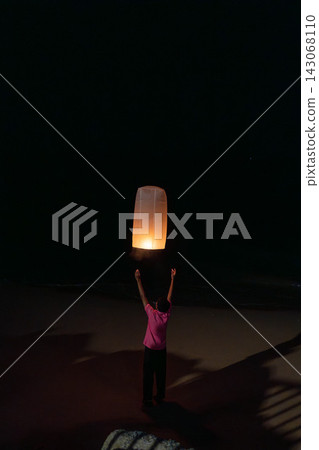Thailand, Khao Lak, December 31, 2025: Young man releasing glowing paper sky lantern at night during festival, warm flame inside lantern lighting his hands, night sky background with soft bokeh lights Thailand, Khao Lak, December 31, 2025: Young man releasing glowing paper sky lantern at night during festival, warm flame inside lantern lighting his hands, night sky background with soft bokeh lights 143068110