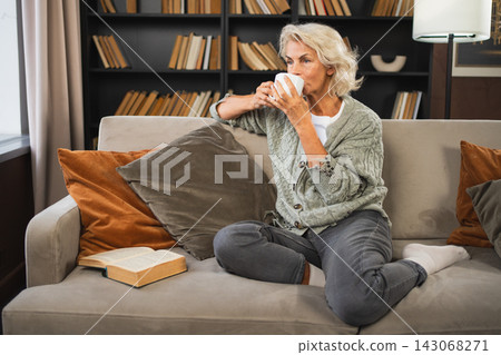 Good morning autumn winter fall vibe. Comfort relaxed senior old elderly woman drinking hot beverage tea coffee in sofa at home. Mature woman resting enjoy calm morning at home alone. Pension concept Good morning autumn winter fall vibe. Comfort relaxed senior old elderly woman drinking hot beverage tea coffee in sofa at home. Mature woman resting enjoy calm morning at home alone. Pension concept 143068271