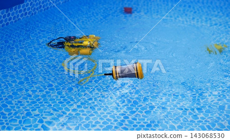 Floating robotic pool cleaner moves across bright blue swimming pool water, with hose, ripples, mosaic tile pattern, and soft reflections suggesting routine maintenance, hygiene, summer comfort, and Floating robotic pool cleaner moves across bright blue swimming pool water, with hose, ripples, mosaic tile pattern, and soft reflections suggesting routine maintenance, hygiene, summer comfort, and 143068530