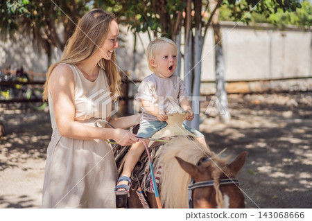 Excited little boy enjoys pony riding with his mother's support. Happy riding experiences and outdoor family fun. Excited little boy enjoys pony riding with his mother's support. Happy riding experiences and outdoor family fun. 143068666
