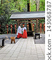 A shrine maiden stands silently in the tranquil temple grounds, her back to the camera. 143068787