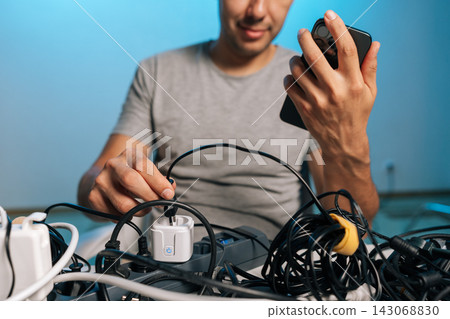 Concept of modern life with many electronic devices, power consumption, cable management challenges. Close-up on hands with cool blue lighting. Concept of modern life with many electronic devices, power consumption, cable management challenges. Close-up on hands with cool blue lighting. 143068830