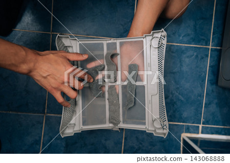 Hands removing lint from tumble dryer filter, highlighting household appliance maintenance and importance of regular cleaning to ensure machine efficiency and safety. Concept of household cleanliness. Hands removing lint from tumble dryer filter, highlighting household appliance maintenance and importance of regular cleaning to ensure machine efficiency and safety. Concept of household cleanliness. 143068888