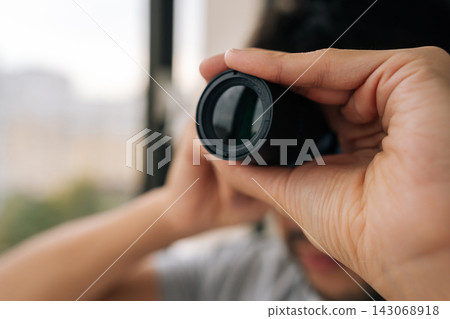 Close-up face of man peers through handheld monocular toward distant landscape, symbolizing focused observation, exploration, discovery and forward-looking planning for research or adventure. Close-up face of man peers through handheld monocular toward distant landscape, symbolizing focused observation, exploration, discovery and forward-looking planning for research or adventure. 143068918