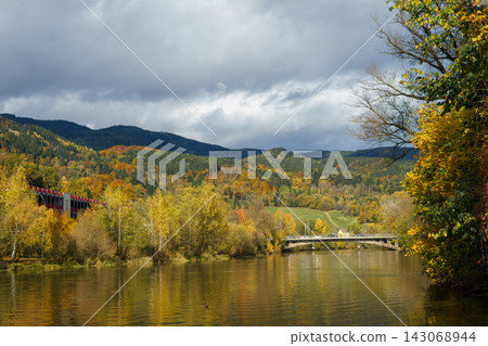 An autumn river flows through a mountain valley beneath a cloudy sky. Concept of nature, landscape, seasonality, travel, tranquility and wilderness An autumn river flows through a mountain valley beneath a cloudy sky. Concept of nature, landscape, seasonality, travel, tranquility and wilderness 143068944