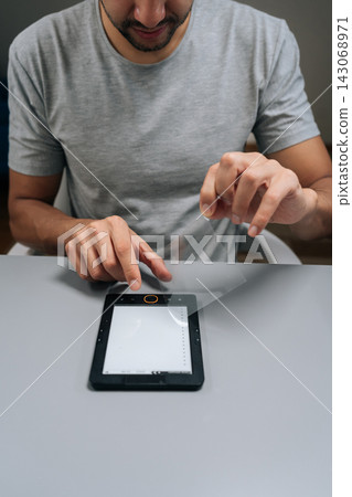Close-up of man applying transparent screen protector film onto black digital e-reader, device for reading electronic books, protecting screen from scratches and damagemale. Close-up of man applying transparent screen protector film onto black digital e-reader, device for reading electronic books, protecting screen from scratches and damagemale. 143068971