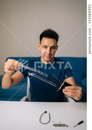 Vertical portrait of man assembling wi-fi module by connecting antennas sitting at white table in home office, focused on ensuring optimal performance for wireless connectivity. 143068991