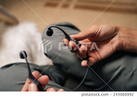 Male hands holding bone-conduction headphones, preparing to listen to music or audiobook outdoors while engaging in activities, offering open-ear listening experience. 143068992