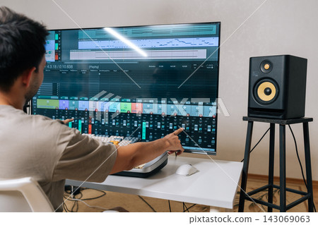 Back view of sound engineer male creating new music in home studio, arranging tracks and mixing audio levels with midi keyboard and software on a large display, showcasing modern music production. Back view of sound engineer male creating new music in home studio, arranging tracks and mixing audio levels with midi keyboard and software on a large display, showcasing modern music production. 143069063