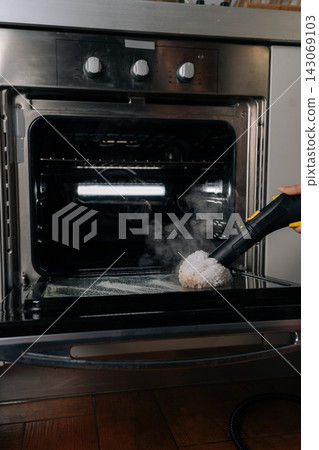 Vertical shot of unrecognizable person removing greasy oven interior with eco-friendly steam cleaner, removing burnt-on food and stains for spotless, sanitary appliance maintenance in kitchen. Vertical shot of unrecognizable person removing greasy oven interior with eco-friendly steam cleaner, removing burnt-on food and stains for spotless, sanitary appliance maintenance in kitchen. 143069103
