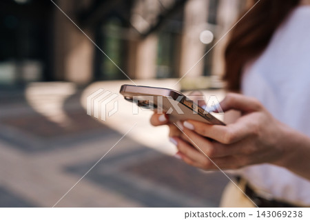 Close-up of woman hands with white manicure holding smartphone. Closeup female texting, browsing social media on city street. Shallow depth of field with warm, natural light and bokeh background. Close-up of woman hands with white manicure holding smartphone. Closeup female texting, browsing social media on city street. Shallow depth of field with warm, natural light and bokeh background. 143069238