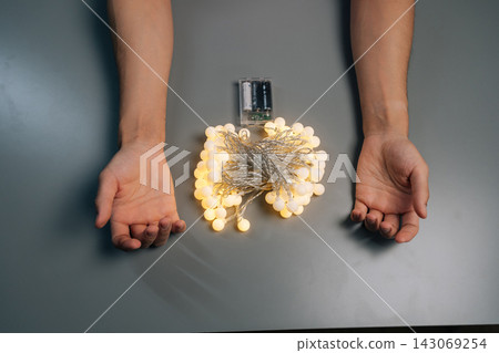 High-angle view of person holding illuminated string lights, preparing home decoration for holiday season, festive event, warm ambient lighting design, creating cozy atmosphere. 143069254