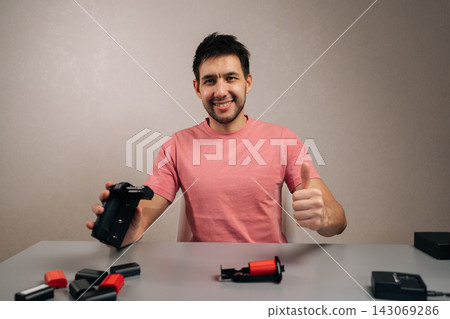 Smiling man presenting camera battery grip and extra batteries, giving thumbs up gesture indicating approval for reliable power solutions and enhanced camera functionality. Smiling man presenting camera battery grip and extra batteries, giving thumbs up gesture indicating approval for reliable power solutions and enhanced camera functionality. 143069286