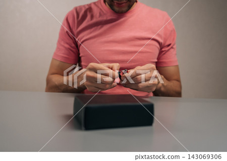 Close-up cropped shot of person using small red multi-tool to open, unbox, and unpack new product gadget from black cardboard packaging box sitting at table, revealing retail technology delivery. Close-up cropped shot of person using small red multi-tool to open, unbox, and unpack new product gadget from black cardboard packaging box sitting at table, revealing retail technology delivery. 143069306