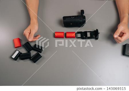High-angle view of filmmaker loading rechargeable battery into black camera grip accessory, preparing for extended shooting sessions and enhanced vertical handling performance, close-up, cropped shot. 143069315