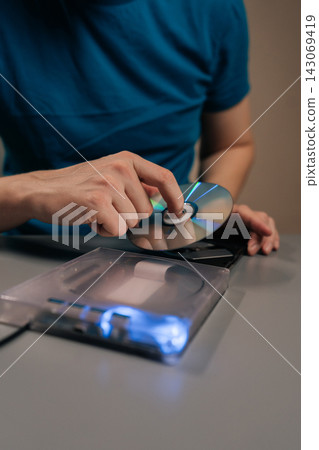 Vertical cropped shot of person interacting with computing hardware, loading data storage disc into portable optical drive, connecting to personal computer for file access, software installation. Vertical cropped shot of person interacting with computing hardware, loading data storage disc into portable optical drive, connecting to personal computer for file access, software installation. 143069419
