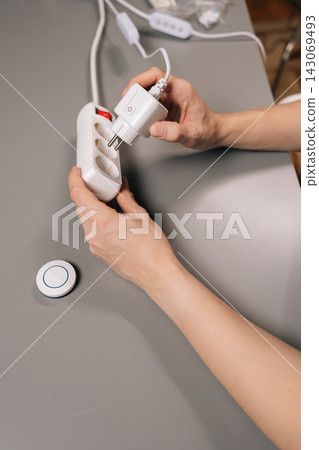 Vertical cropped shot of person inserting smart plug into multi socket power strip, illustrating integration of innovative technology for efficient electricity control and home automation, close-up. Vertical cropped shot of person inserting smart plug into multi socket power strip, illustrating integration of innovative technology for efficient electricity control and home automation, close-up. 143069493