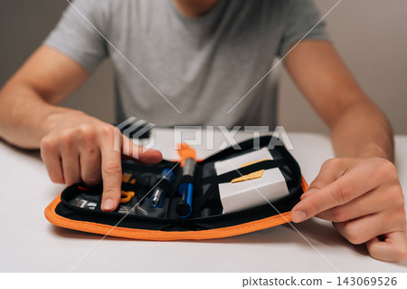 Hands checking soldering iron set with small circuit, preparing precise electronic repair or assembly with open toolkit of components and hand tools on white tabletop, close-up cropped shot. Hands checking soldering iron set with small circuit, preparing precise electronic repair or assembly with open toolkit of components and hand tools on white tabletop, close-up cropped shot. 143069526
