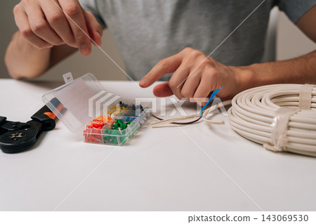 Electrician hands preparing electrical wiring for installation, selecting colorful wire ferrules from organizer box for crimping on cables, performing professional repair work. Electrician hands preparing electrical wiring for installation, selecting colorful wire ferrules from organizer box for crimping on cables, performing professional repair work. 143069530