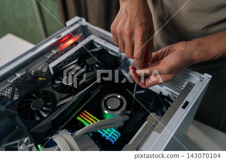 Hands of computer technician using screwdriver to assemble and service internal components of desktop pc, performing maintenance and upgrade tasks on hardware. Concept of desktop PC service. Hands of computer technician using screwdriver to assemble and service internal components of desktop pc, performing maintenance and upgrade tasks on hardware. Concept of desktop PC service. 143070104