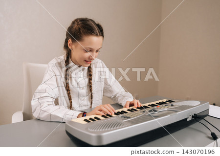 Portrait of happy young girl with pigtails smiling sitting at table, playing digital keyboard synthesizer, engaging in musical practice and expressing creativity. 143070196