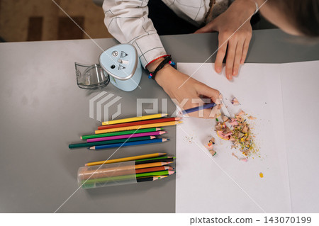 High-angle view of child hands holding blue colored pencil drawing on white paper, surrounded by sharpened vibrant pencils and shavings on desk creative childhood learning and artistic development. 143070199