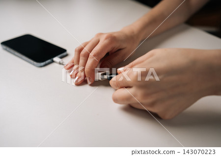 Close-up hands of unrecognizable woman connecting USB flash drive to smartphone through adapter cable, facilitating data transfer and expanding mobile storage sitting on white table, closeup. Close-up hands of unrecognizable woman connecting USB flash drive to smartphone through adapter cable, facilitating data transfer and expanding mobile storage sitting on white table, closeup. 143070223
