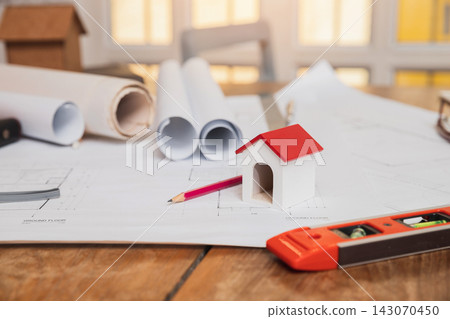 Architects house model with measurement tool and blueprints on architect desk. A architects home model with plan and blueprints. Business, architecture, building and construction concept. Architects house model with measurement tool and blueprints on architect desk. A architects home model with plan and blueprints. Business, architecture, building and construction concept. 143070450