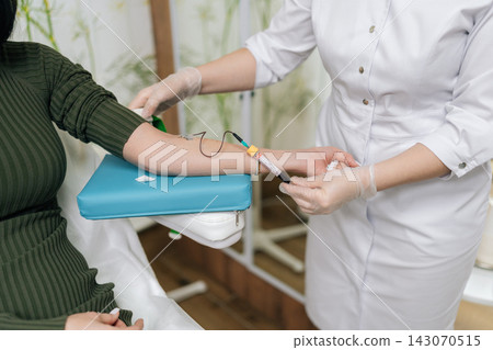 Close-up of phlebotomist in clinic drawing blood from woman arm for health exam, then removing butterfly needle and applying cotton swab to venipuncture site while wearing gloves. Close-up of phlebotomist in clinic drawing blood from woman arm for health exam, then removing butterfly needle and applying cotton swab to venipuncture site while wearing gloves. 143070515