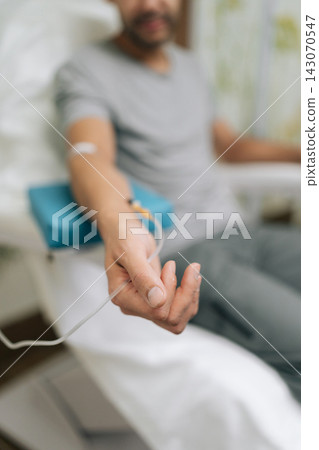 Close-up male arm resting on medical padded support while receiving intravenous drip, delivering essential vitamins and medication directly into bloodstream for health and wellness. Close-up male arm resting on medical padded support while receiving intravenous drip, delivering essential vitamins and medication directly into bloodstream for health and wellness. 143070547
