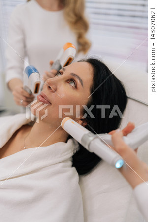 Close-up vertical portrait of woman receiving various professional aesthetic treatments including ultrasound and advanced devices by cosmetologists for skin care and rejuvenation in beauty clinic. Close-up vertical portrait of woman receiving various professional aesthetic treatments including ultrasound and advanced devices by cosmetologists for skin care and rejuvenation in beauty clinic. 143070621