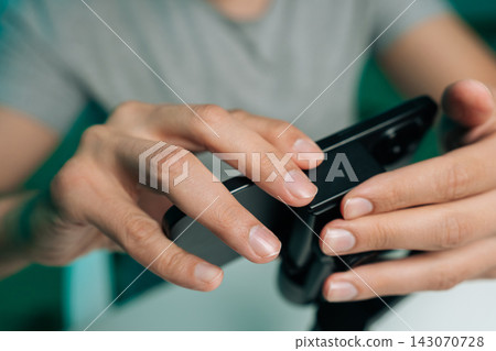 Person hands closely interacting with mobile device. Concept of fingers on screen and controls. Concept of modern technology engagement, online gaming, digital communication trends. Person hands closely interacting with mobile device. Concept of fingers on screen and controls. Concept of modern technology engagement, online gaming, digital communication trends. 143070728