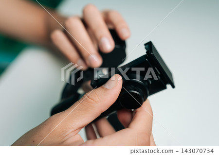 Hands adjusting black camera accessories, securing smartphone stabilizer to tripod head, setting up electronic gear for content creation and videography, close-up, cropped shot. Hands adjusting black camera accessories, securing smartphone stabilizer to tripod head, setting up electronic gear for content creation and videography, close-up, cropped shot. 143070734