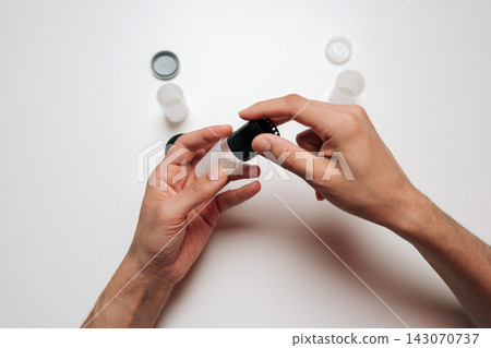 Person hands manipulating classic 35mm film roll, placing it inside translucent plastic canister for protection, organization against clean white background. Person hands manipulating classic 35mm film roll, placing it inside translucent plastic canister for protection, organization against clean white background. 143070737