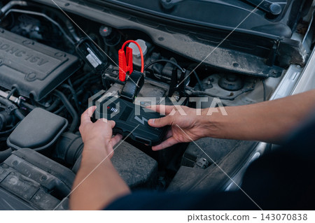 Male hands connect portable power bank jump starter to car battery. Emergency roadside assistance, automotive service, modern vehicle maintenance or problem solving concept. Male hands connect portable power bank jump starter to car battery. Emergency roadside assistance, automotive service, modern vehicle maintenance or problem solving concept. 143070838